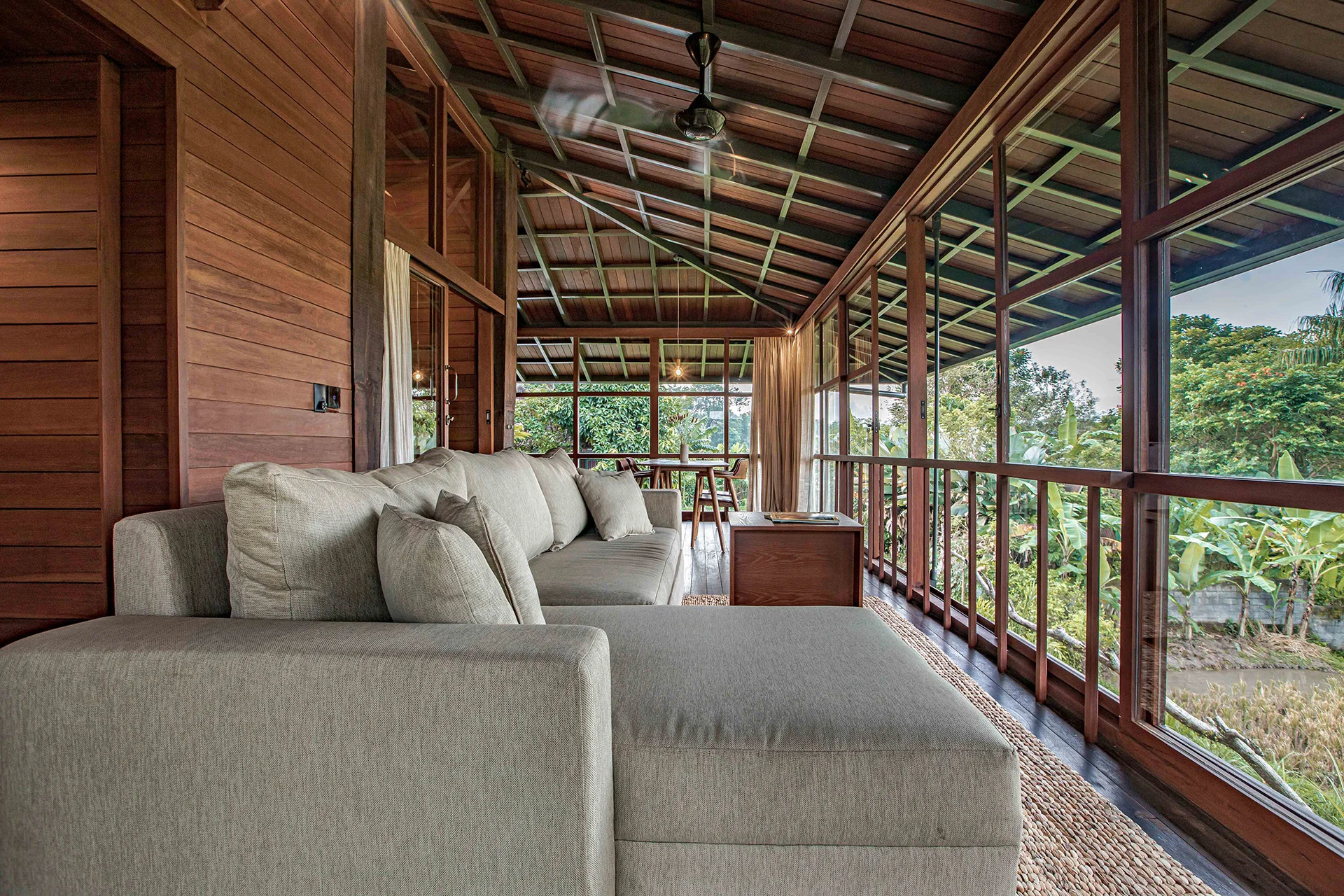 The treehouse lounge, a grey sofa against timber walls under a dark timber ceiling, glazing on two sides open to the greenery